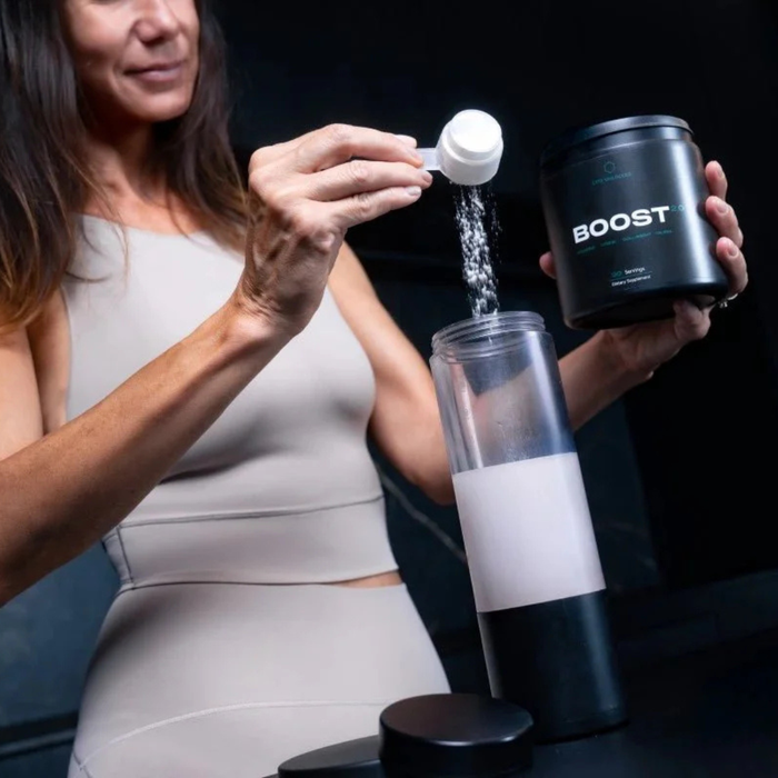 Woman adding powder from a container labeled 'Boost' into a shaker bottle.
