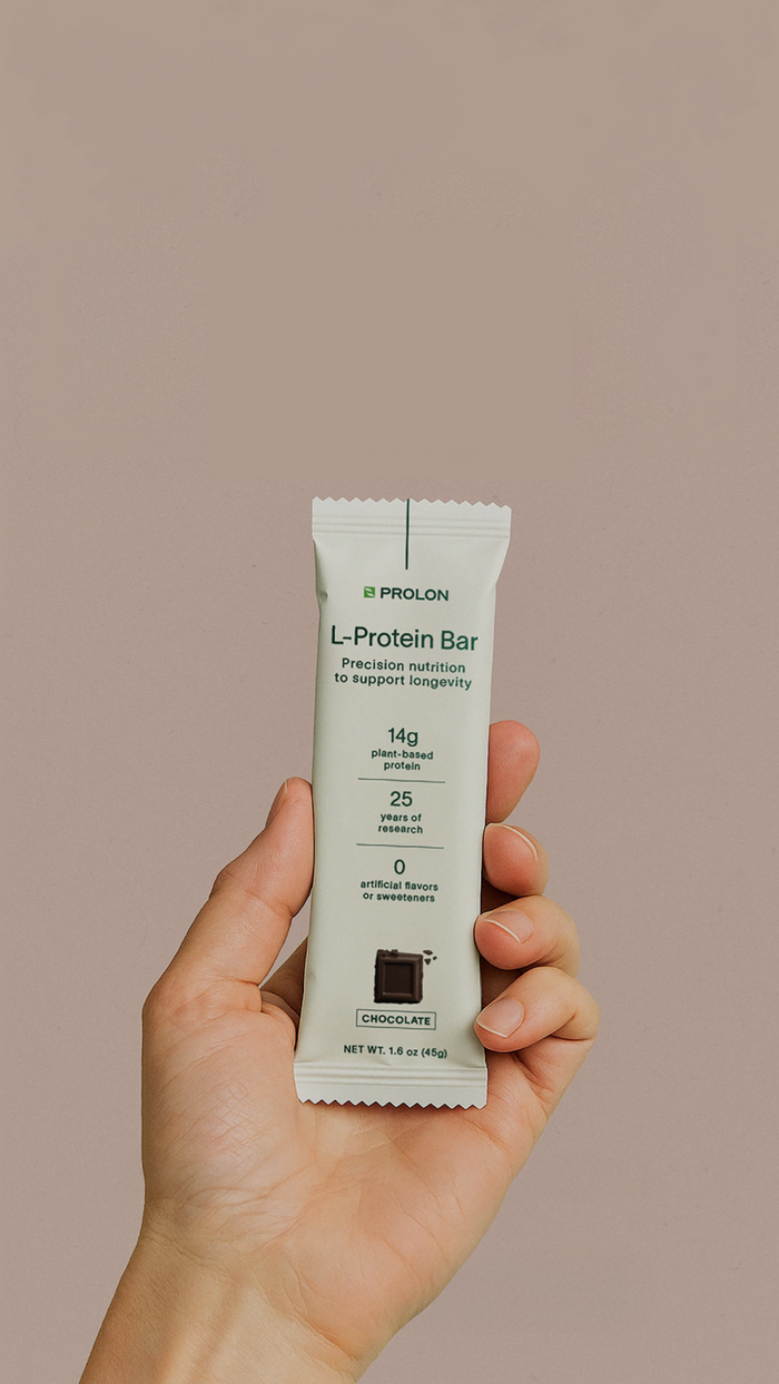 Hand holding a L-Protein Bar package against a beige background